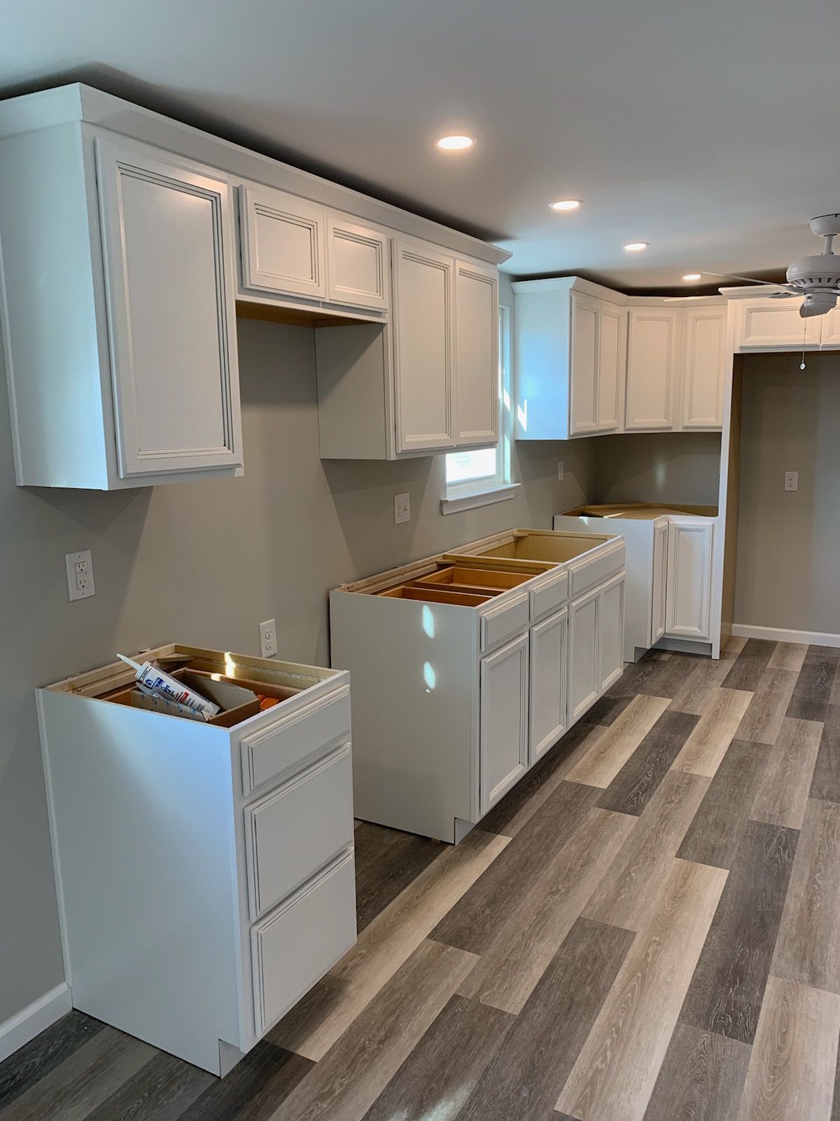 Kitchen with white cabinets, gray walls, and wood-look flooring, with drawers and countertops covered in boxes.