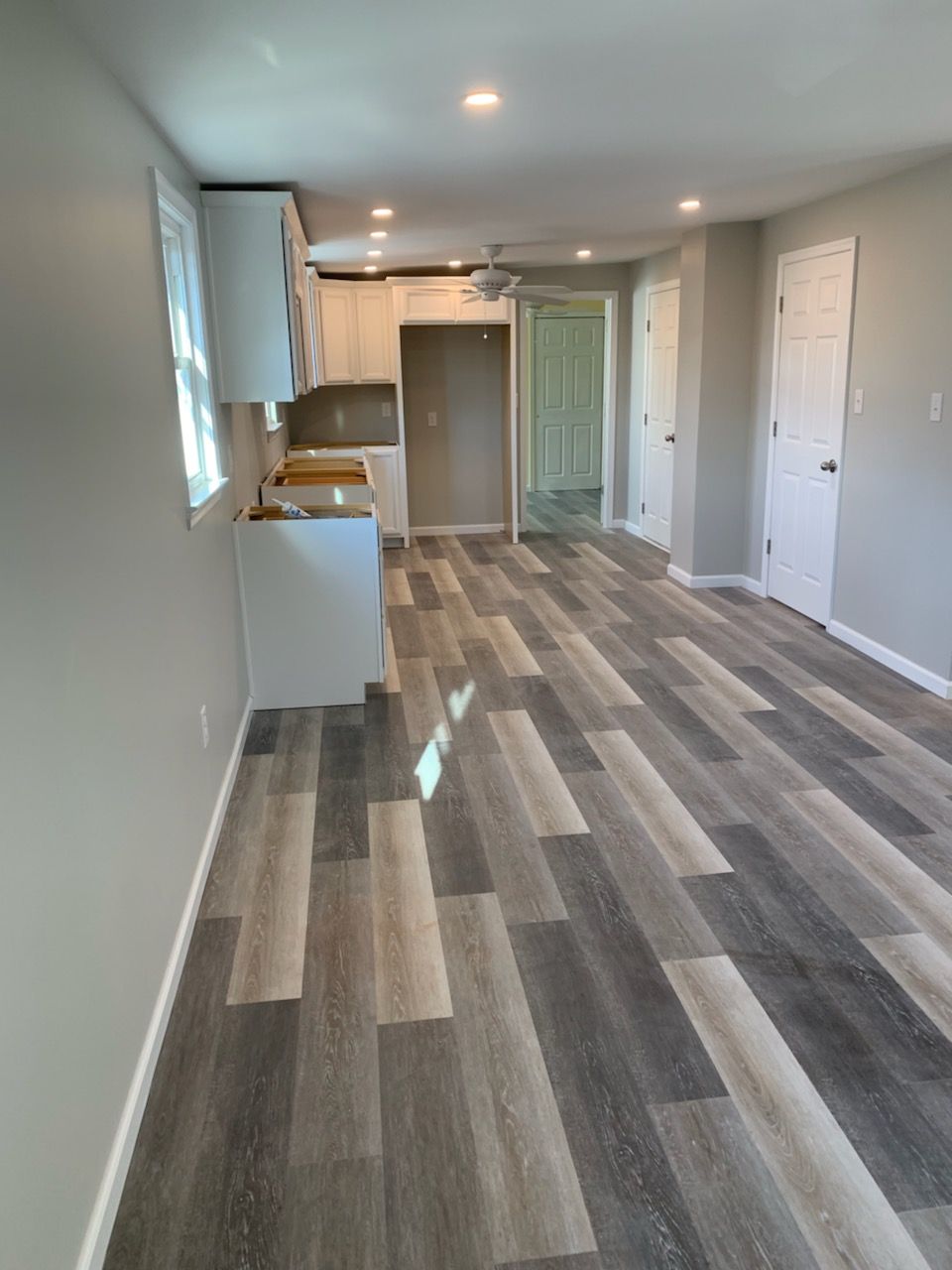 Empty modern apartment living area with gray wood flooring, white walls, and a small kitchen.