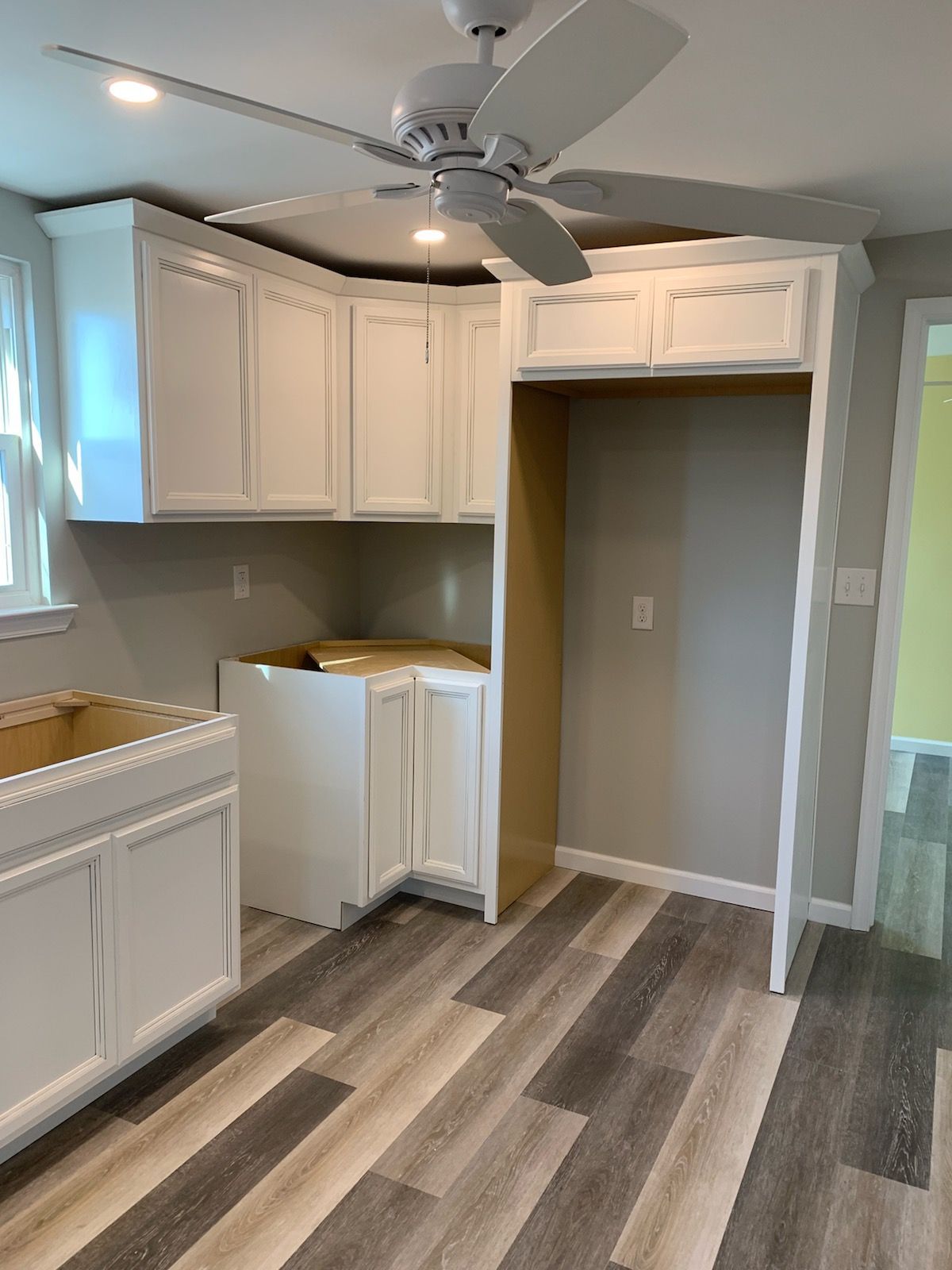 Small laundry room with white cabinets, sink, ceiling fan, and wood-look flooring.