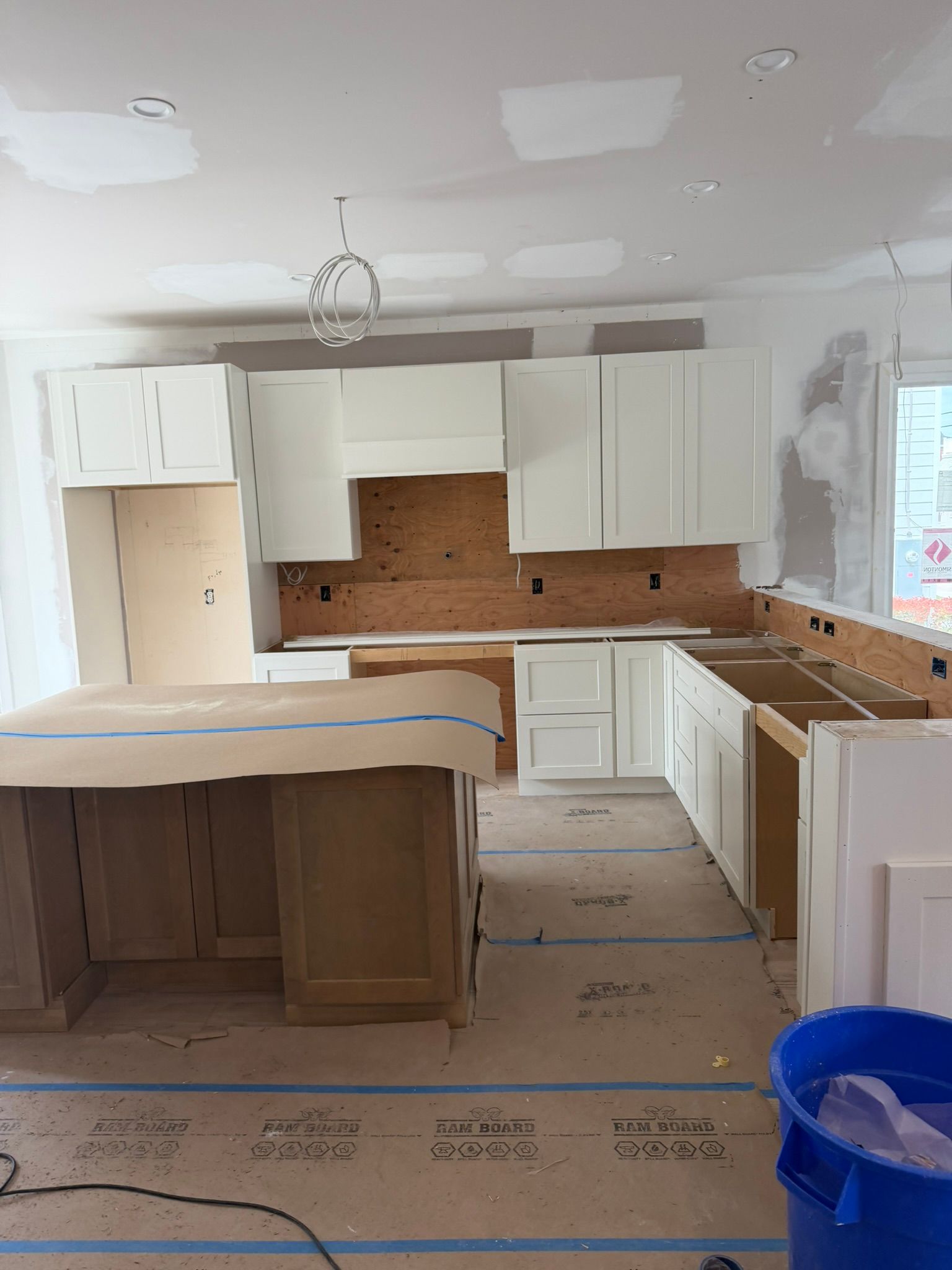 Unfinished kitchen with white cabinets, wood countertops, and drywall in progress.