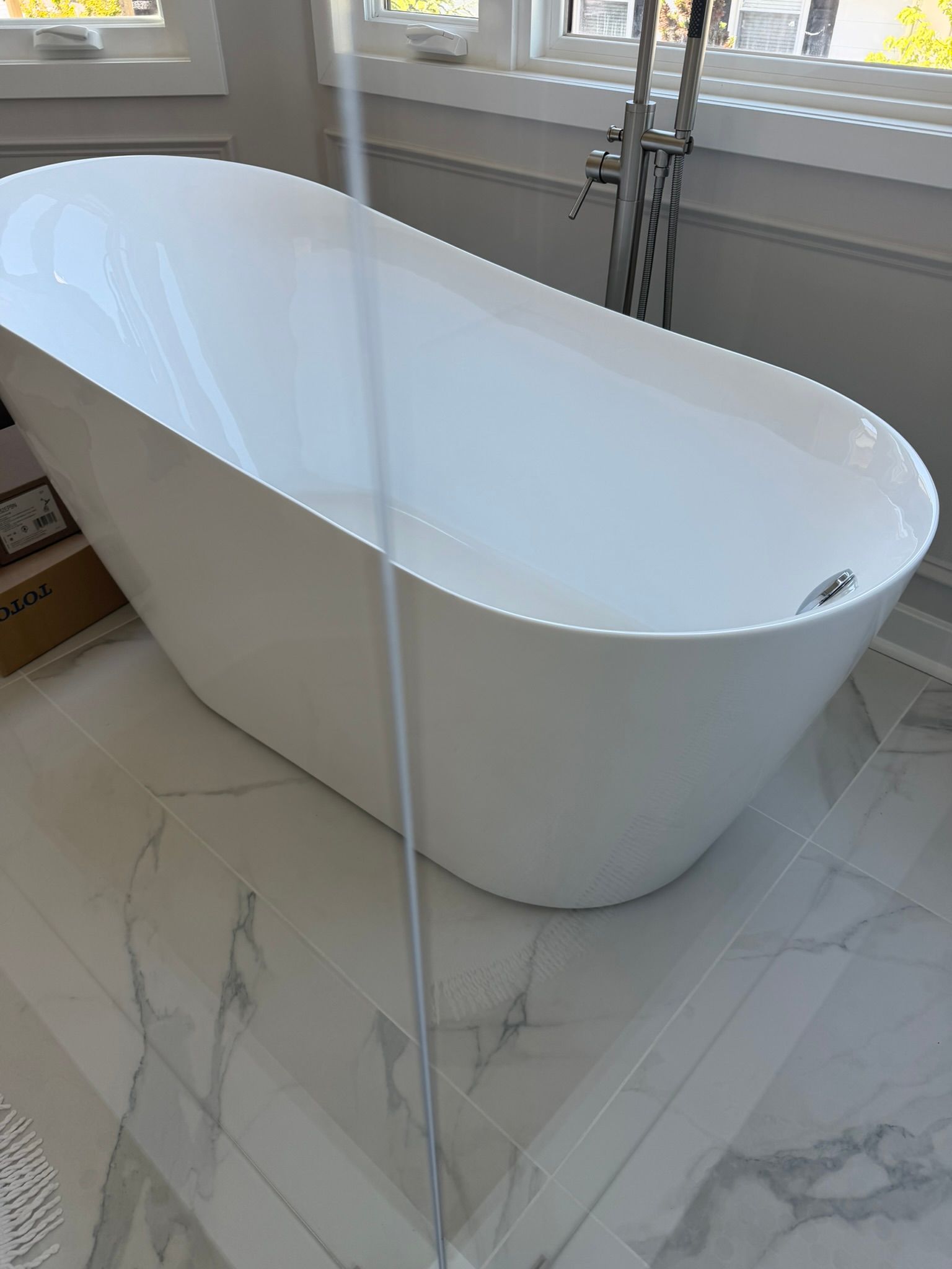 White freestanding bathtub by a window in a bright marble bathroom