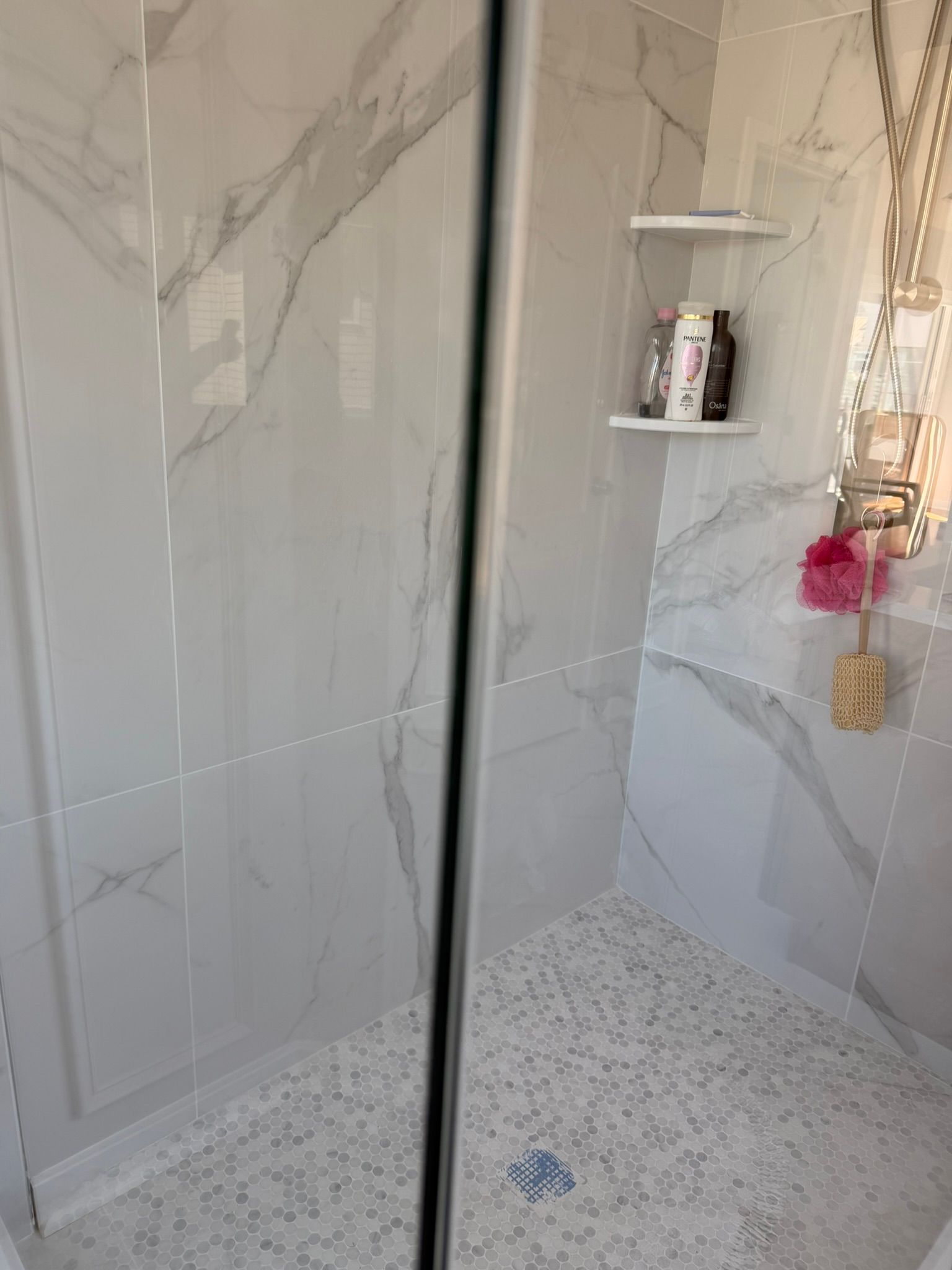 Marble-tiled shower with glass door, gray walls, and a shower shelf holding toiletries.