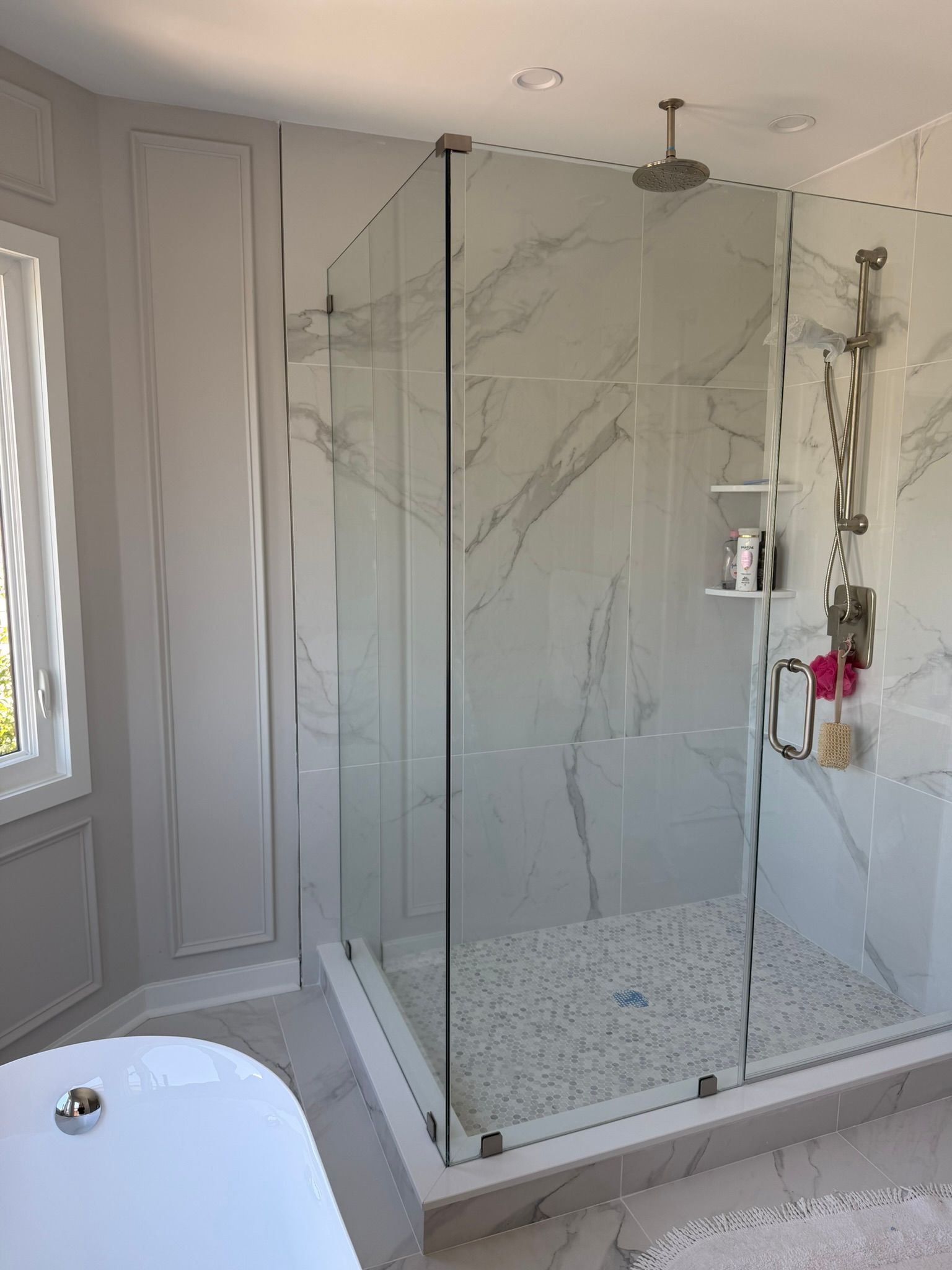 Modern bathroom with glass walk-in shower, marble walls, and a partial view of a bathtub.
