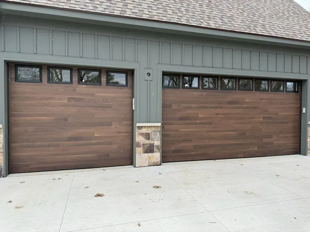 Two-car garage with brown wood-look doors, gray siding, and a concrete driveway