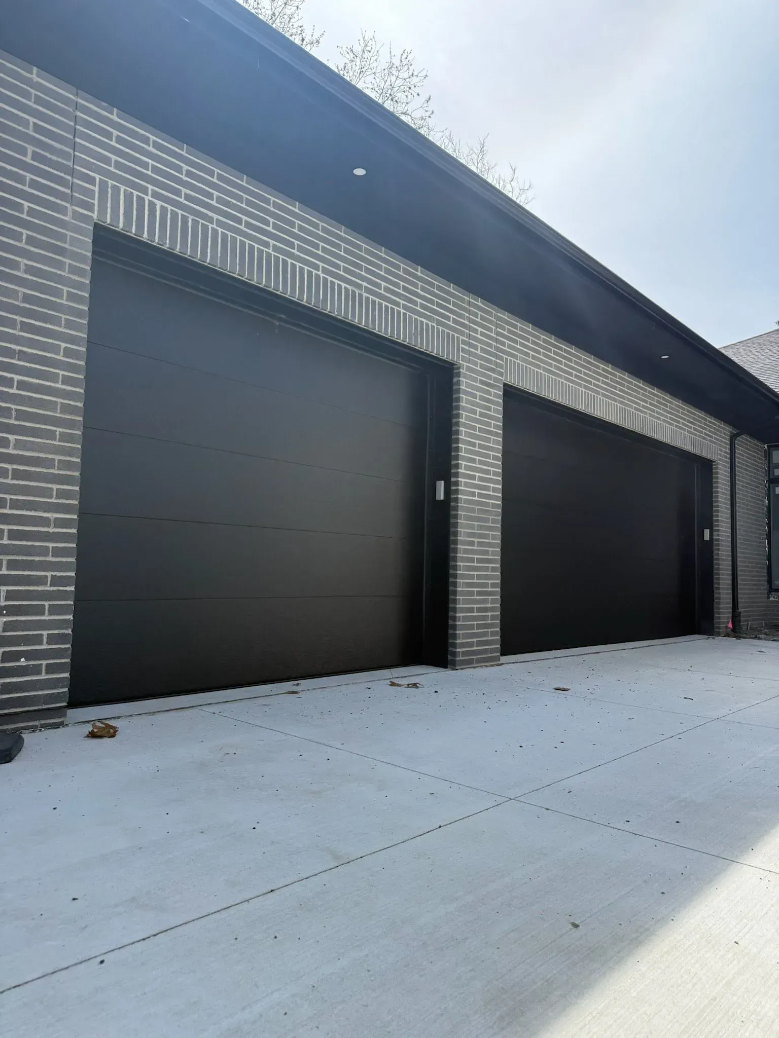 Modern garage exterior with two black doors, gray brick trim, and snow-covered concrete.