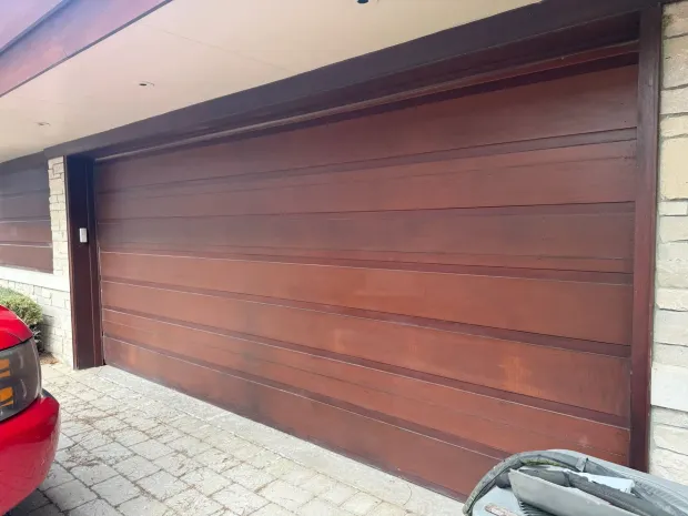 Wooden garage door with horizontal slats beside a driveway and a red car