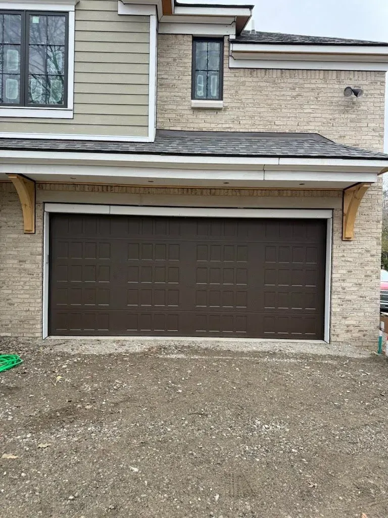 Brown garage door on a beige house exterior with stone siding and a gravel driveway