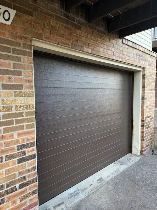 Brown garage door set in a brick exterior under a covered driveway.