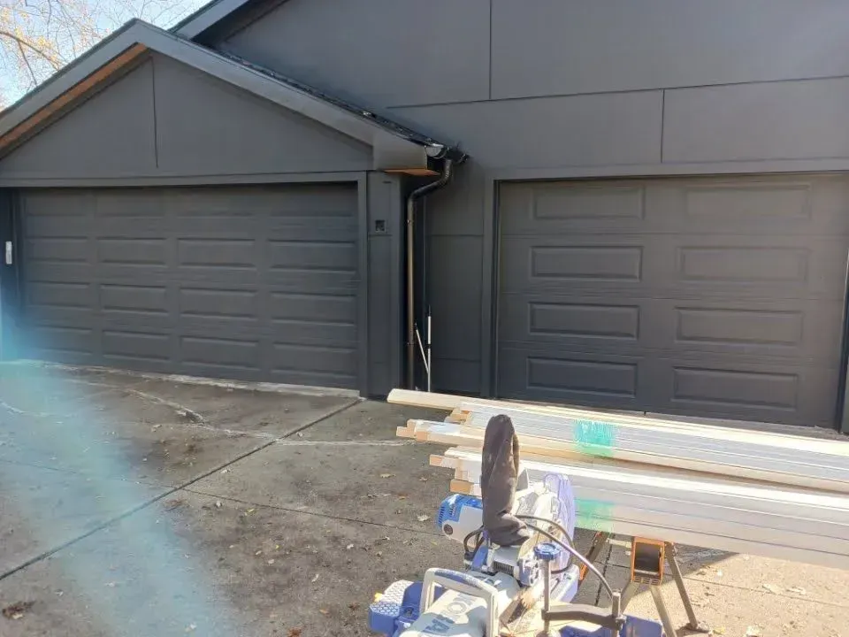 Driveway with two gray garage doors, concrete surface, and construction materials in front.