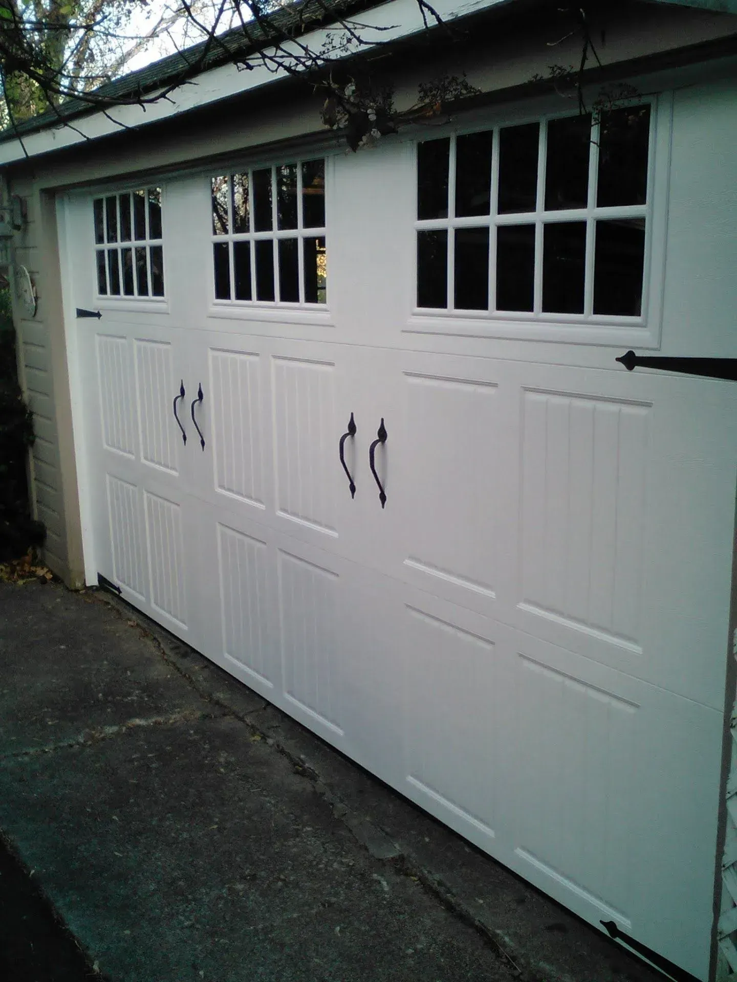 White garage door with windows and black handles on a driveway.