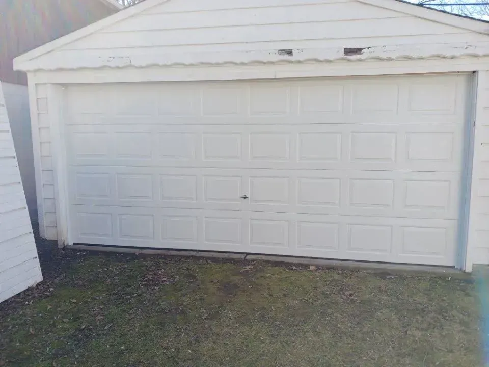 White detached garage with a closed paneled door and small grass lawn in front