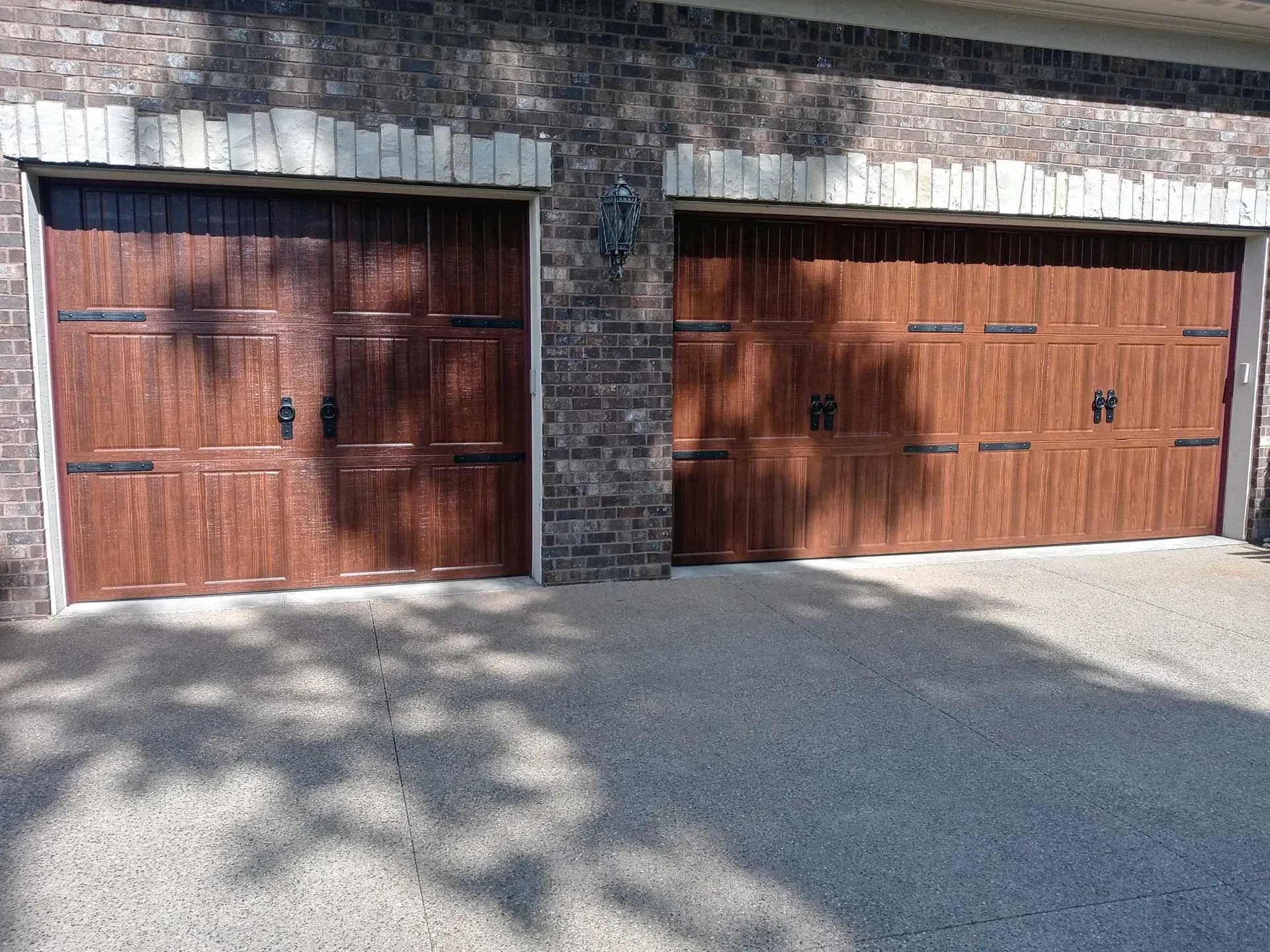 Two wooden garage doors in a stone-and-stucco wall with sunlight and tree shadows on the driveway