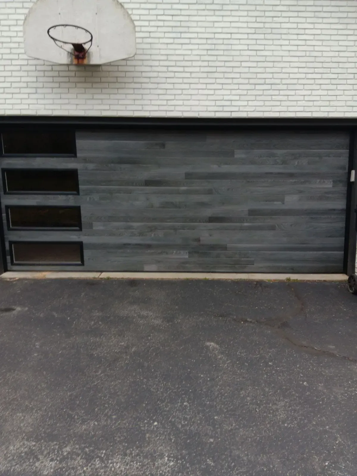 Brick wall with a basketball hoop above a gray garage door.