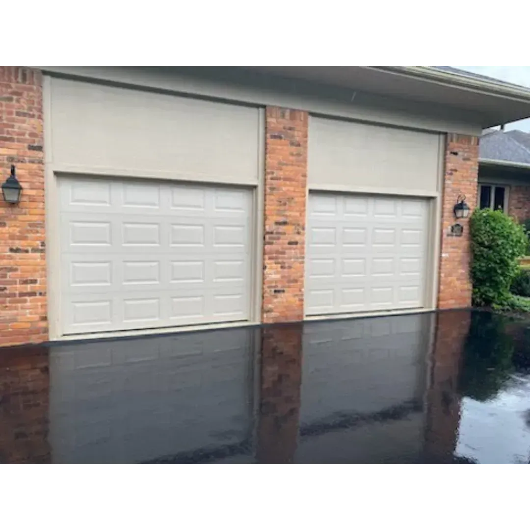 Two white garage doors on a brick house, reflected in a wet driveway.