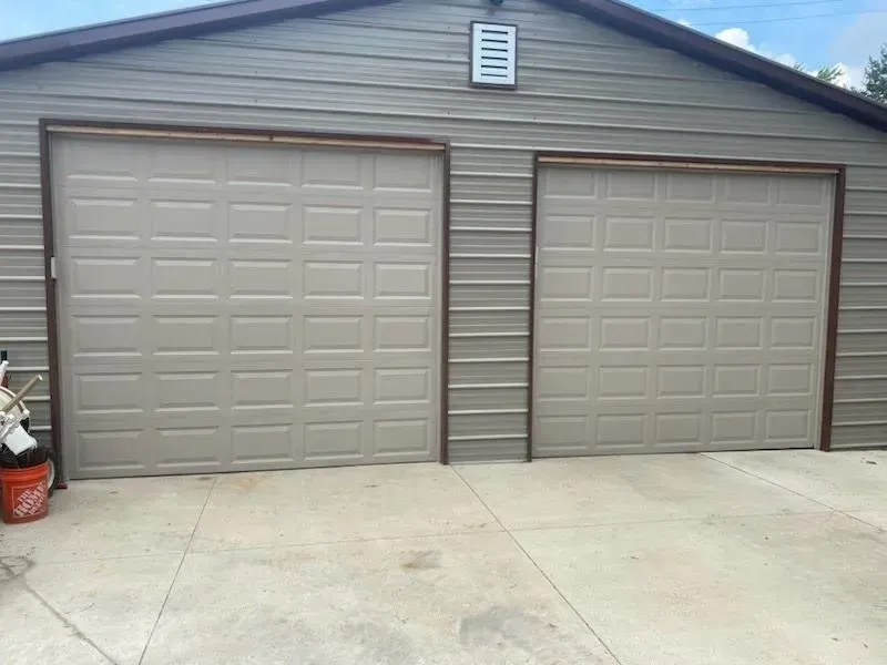 Two beige garage doors on a house exterior with a concrete driveway
