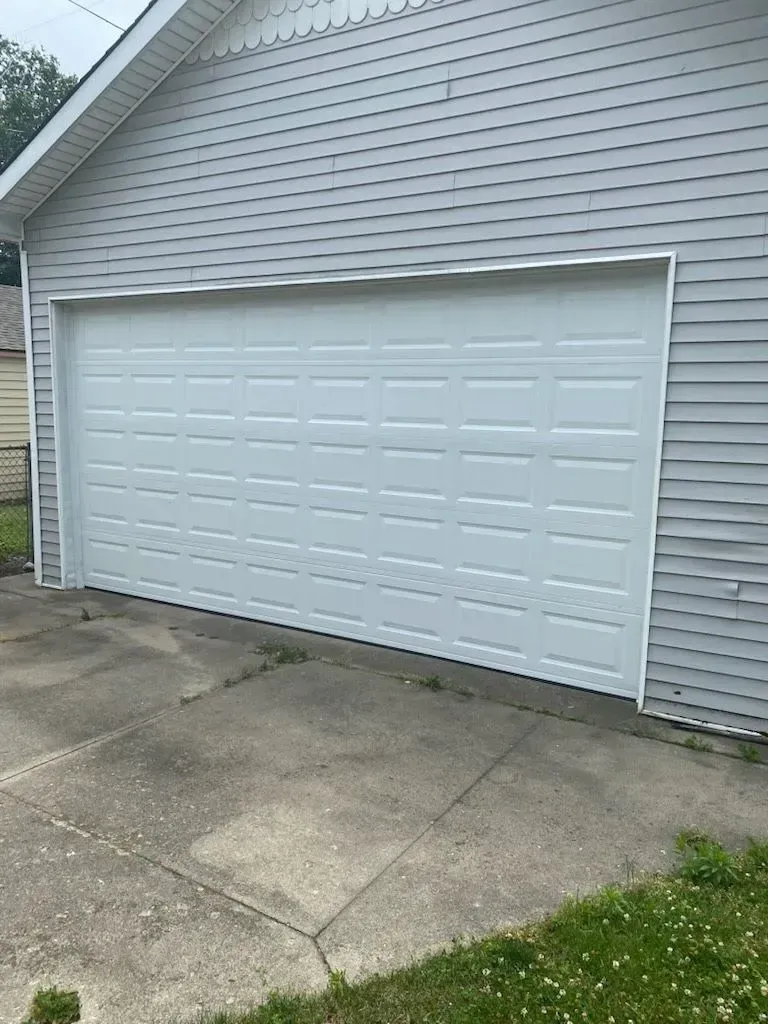 White double garage door on a light gray house with a concrete driveway in front.