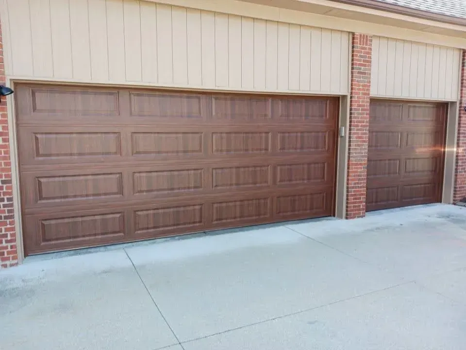 Brown garage doors on a brick-and-beige building with a concrete driveway in front