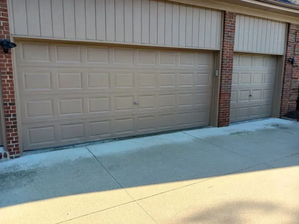 Two beige garage doors beside a brick column in front of a residential building