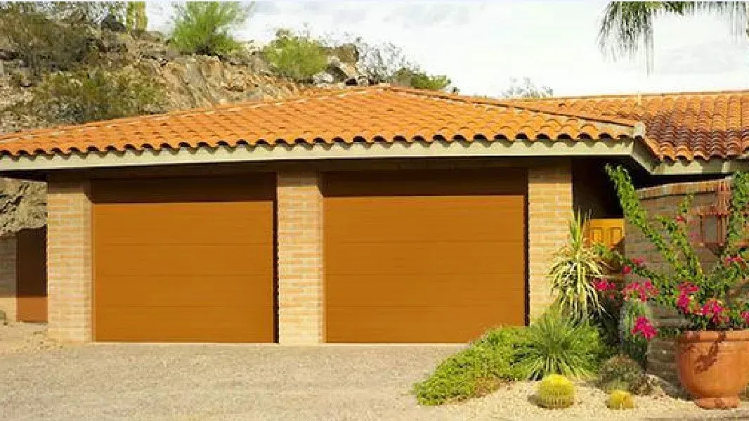 Adobe-style house with two orange garage doors and a terracotta tile roof, surrounded by desert landscaping
