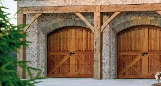 Double wooden garage doors with stone frame and timber beams on a house exterior