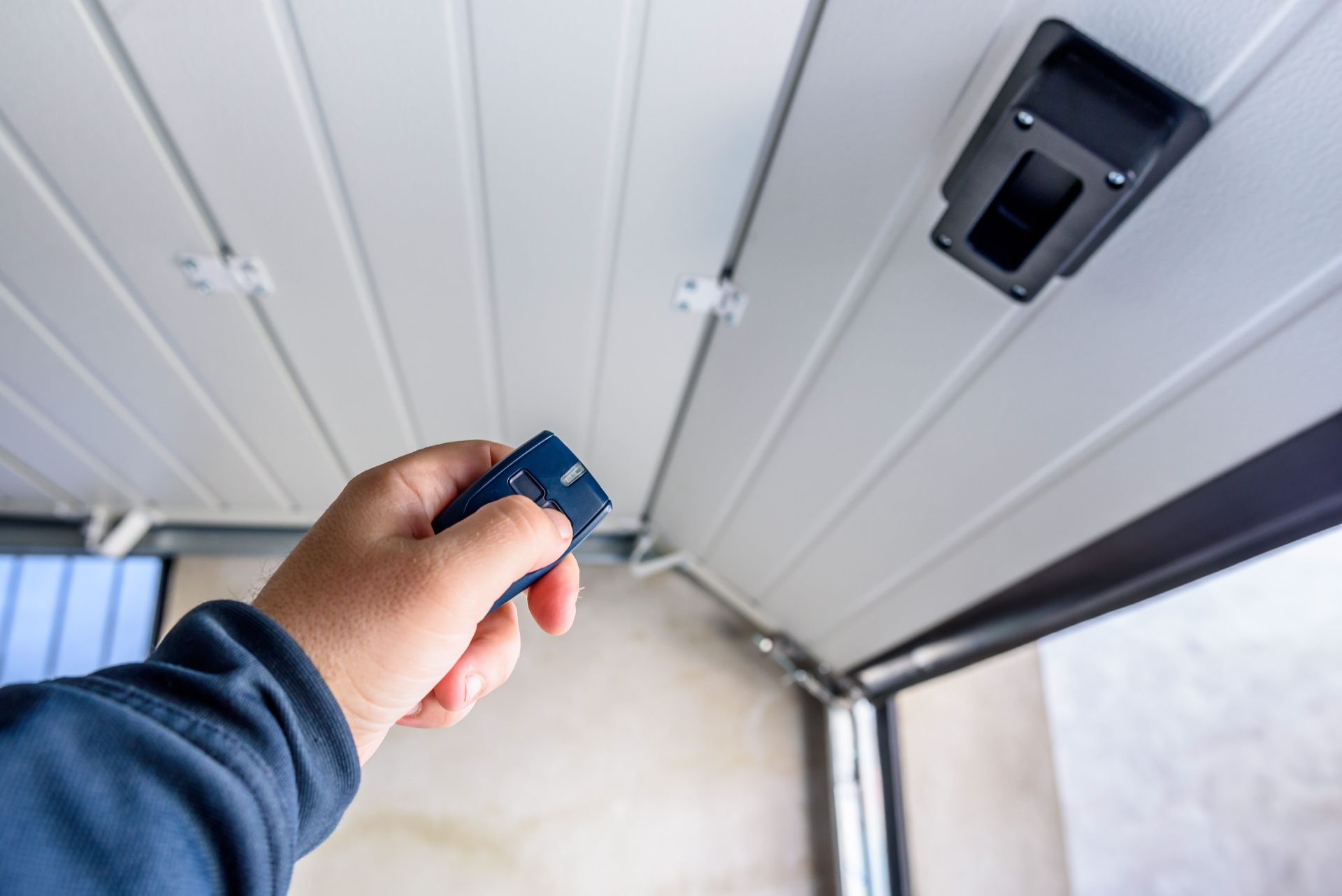 Hand holding a blue garage door remote near a white garage door opener switch