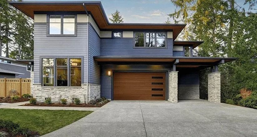 Modern two-story gray house with wood garage doors, large windows, and a wide concrete driveway