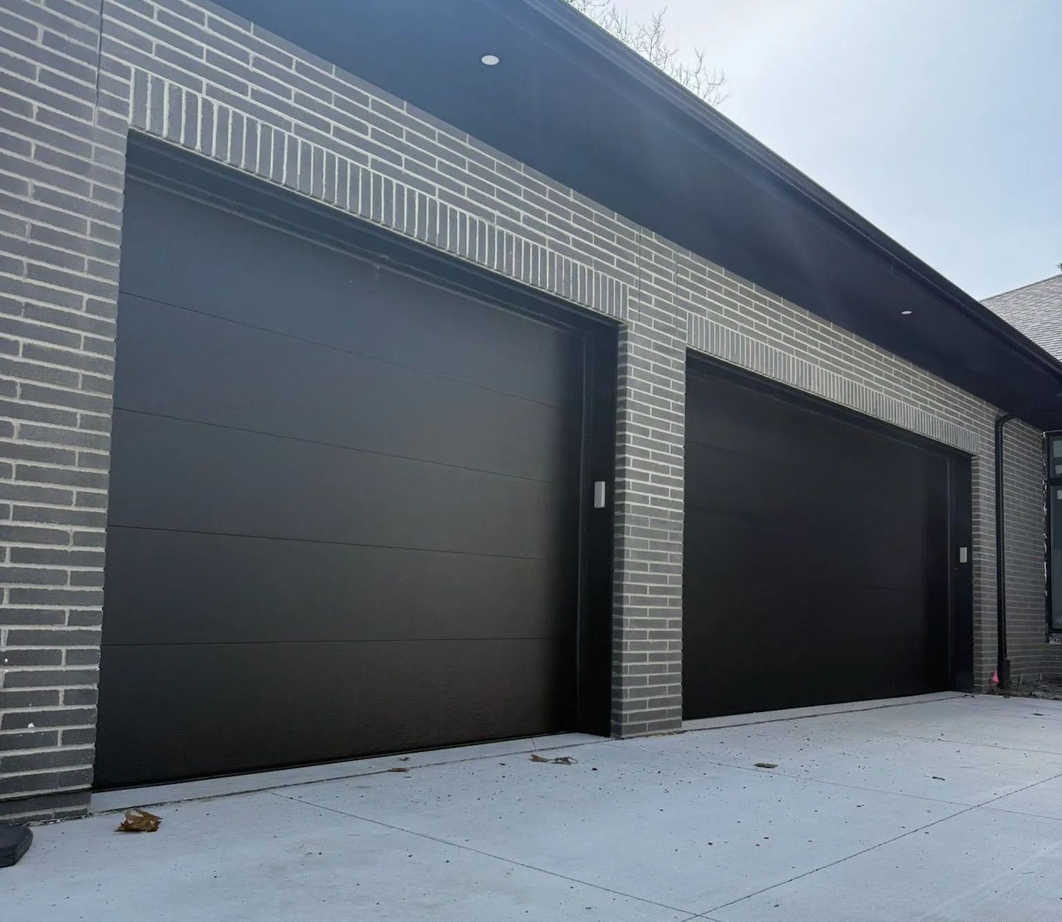 Two black garage doors on a gray brick house with a concrete driveway