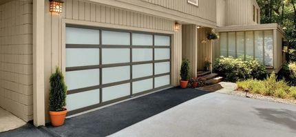 Modern home exterior with a frosted glass garage door, front walkway, and potted plants