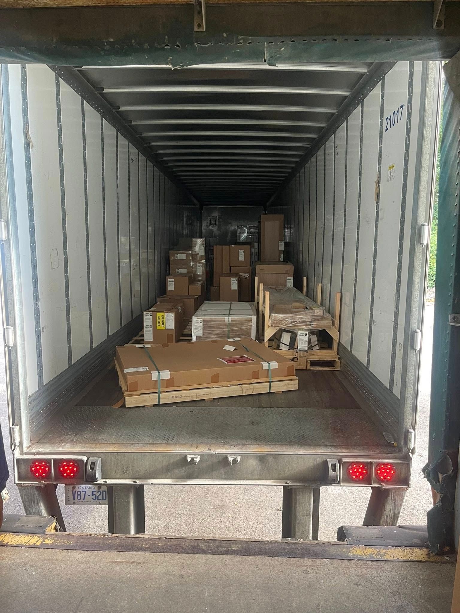 Inside of a cargo trailer filled with cardboard boxes and wooden pallets.