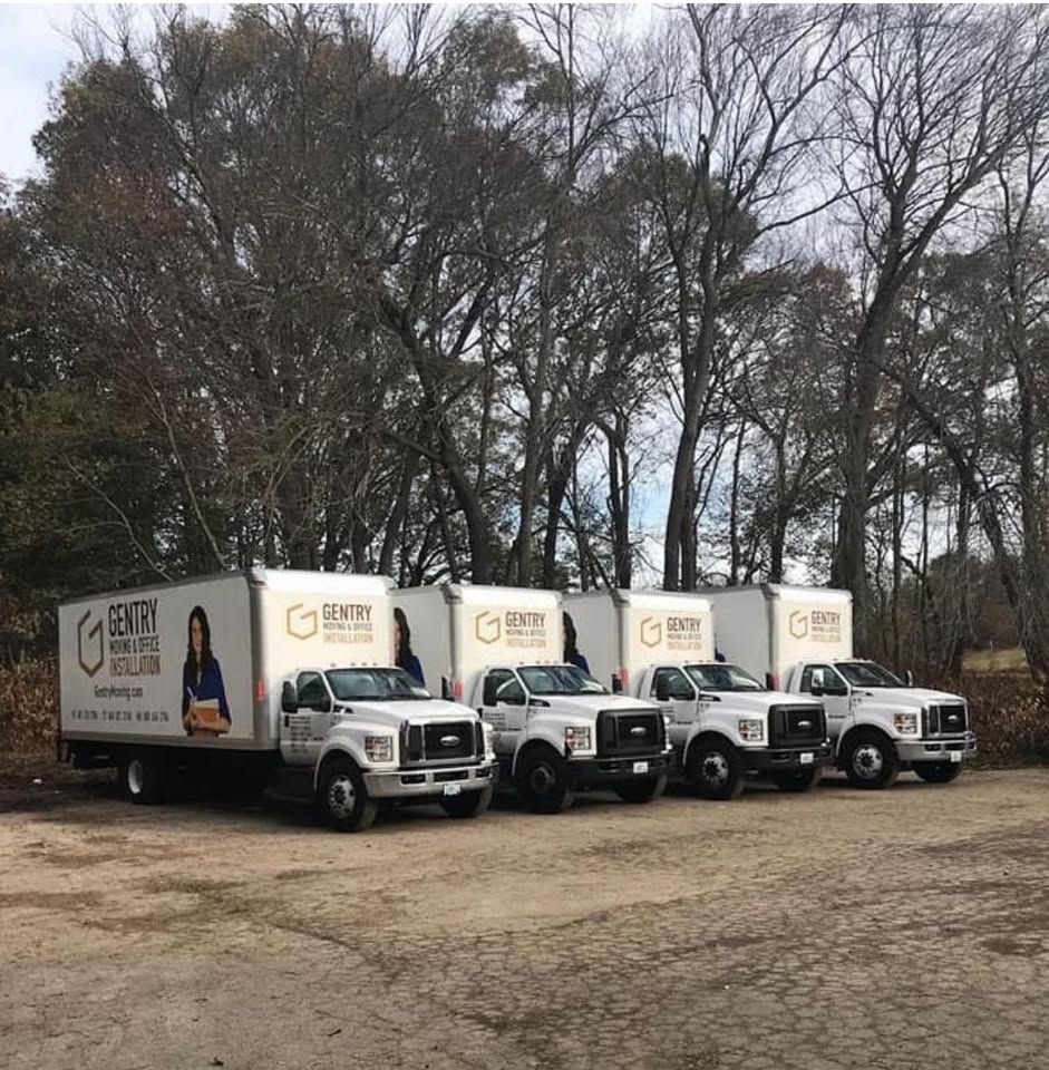 Five white delivery trucks with company logo parked in front of bare trees.