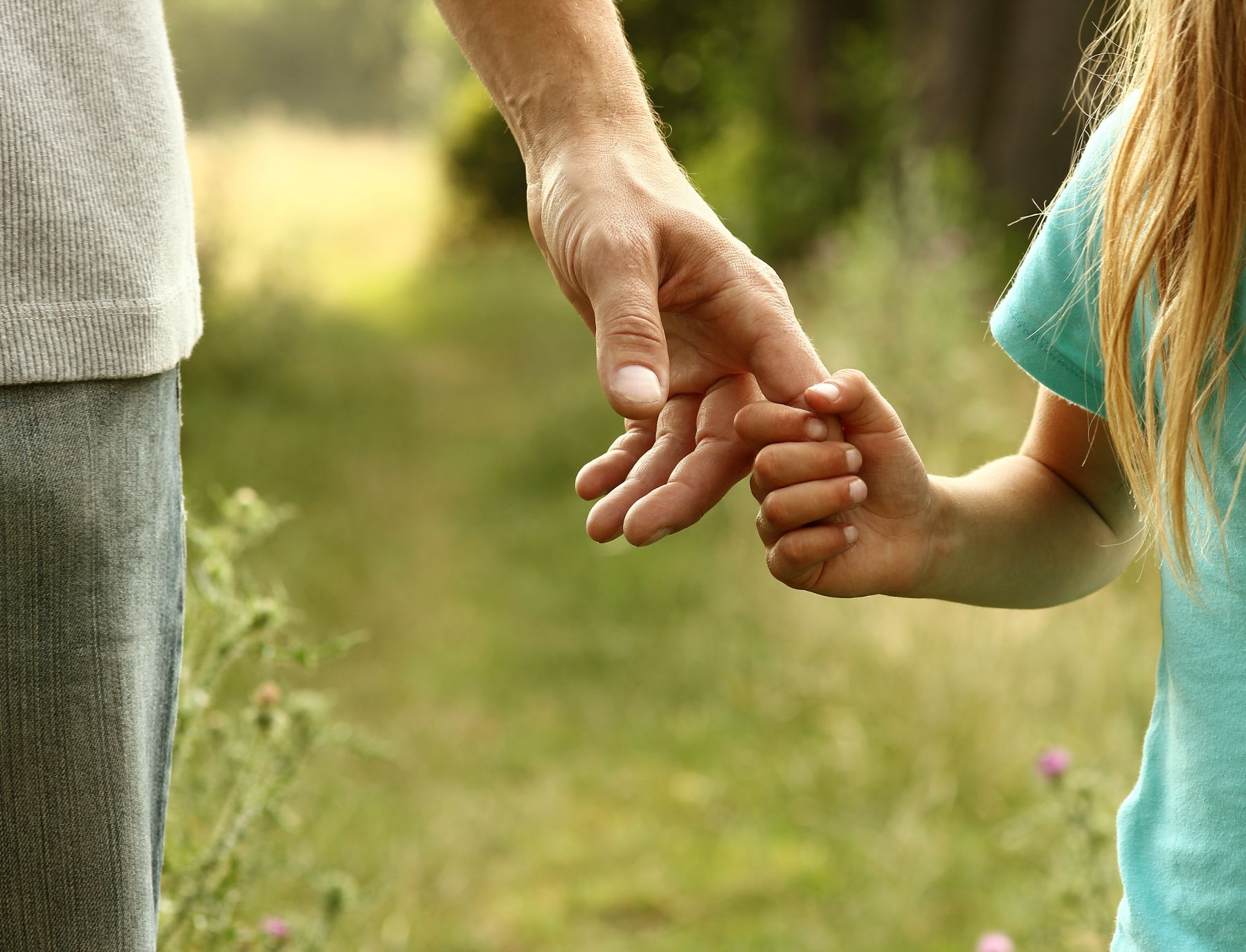 A man and a little girl are holding hands in a field.