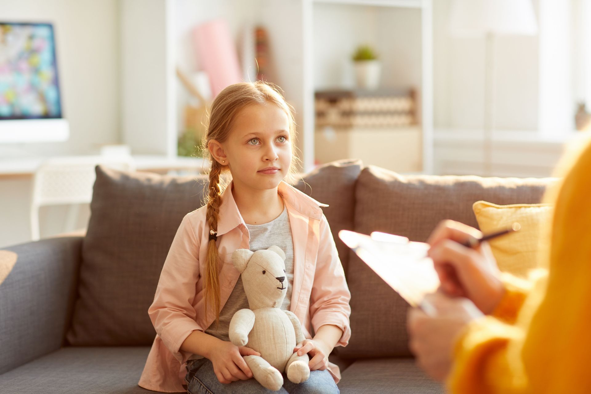 A little girl is sitting on a couch holding a teddy bear.