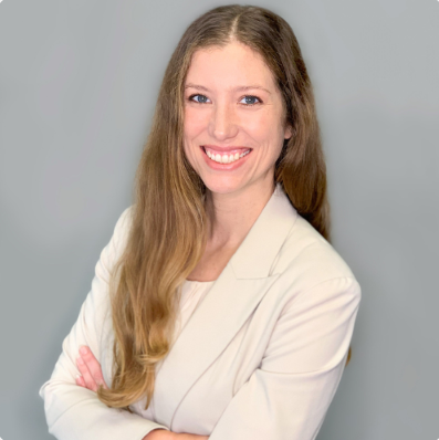 A woman in a white jacket is smiling with her arms crossed.