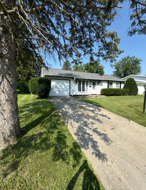 Green lawn in front of a brick house with lush landscaping and a bright blue sky.
