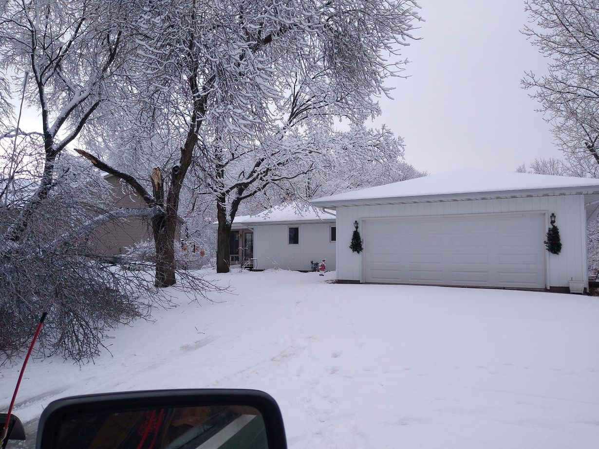 A snow-covered suburban house and yard with heavy snow on the trees, viewed from inside a car.