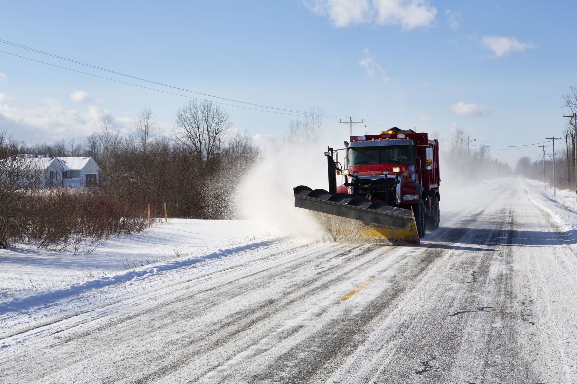 A red snowplow clears a snow-covered road on a sunny day.