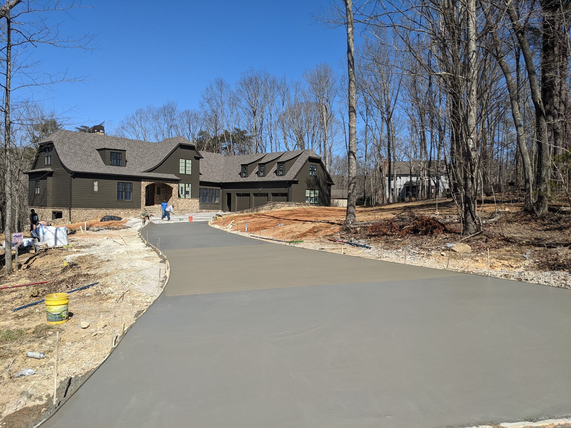 A concrete driveway leading to a large house in the woods.