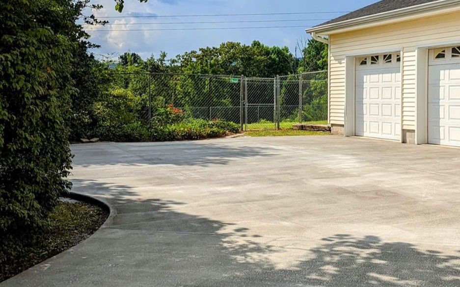 A concrete driveway leading to a garage with a chain link fence in the background.