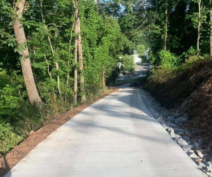A concrete road going through a forest with trees on both sides.