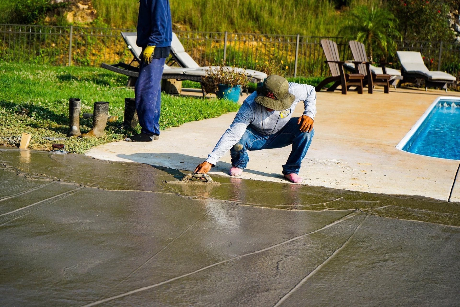 Two men are working on a concrete patio next to a pool.