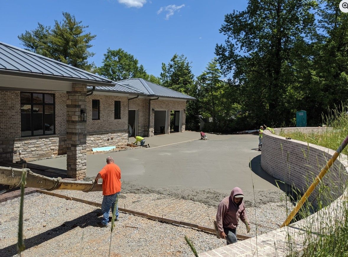 Two men are working on a driveway in front of a house