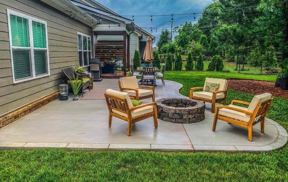 A patio with a fire pit and chairs in front of a house.