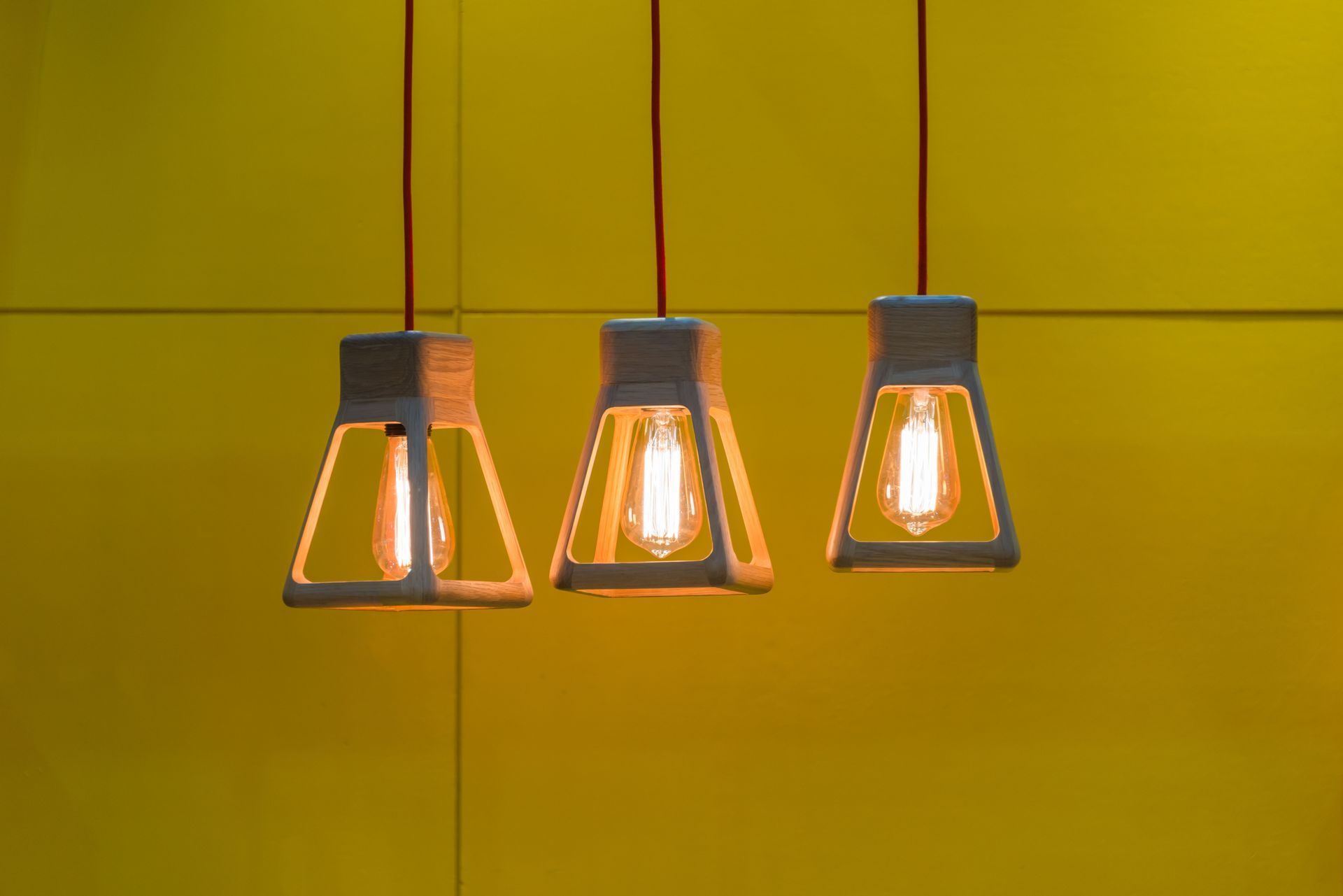 Three pendant lights with Edison bulbs hang in front of a yellow wall.