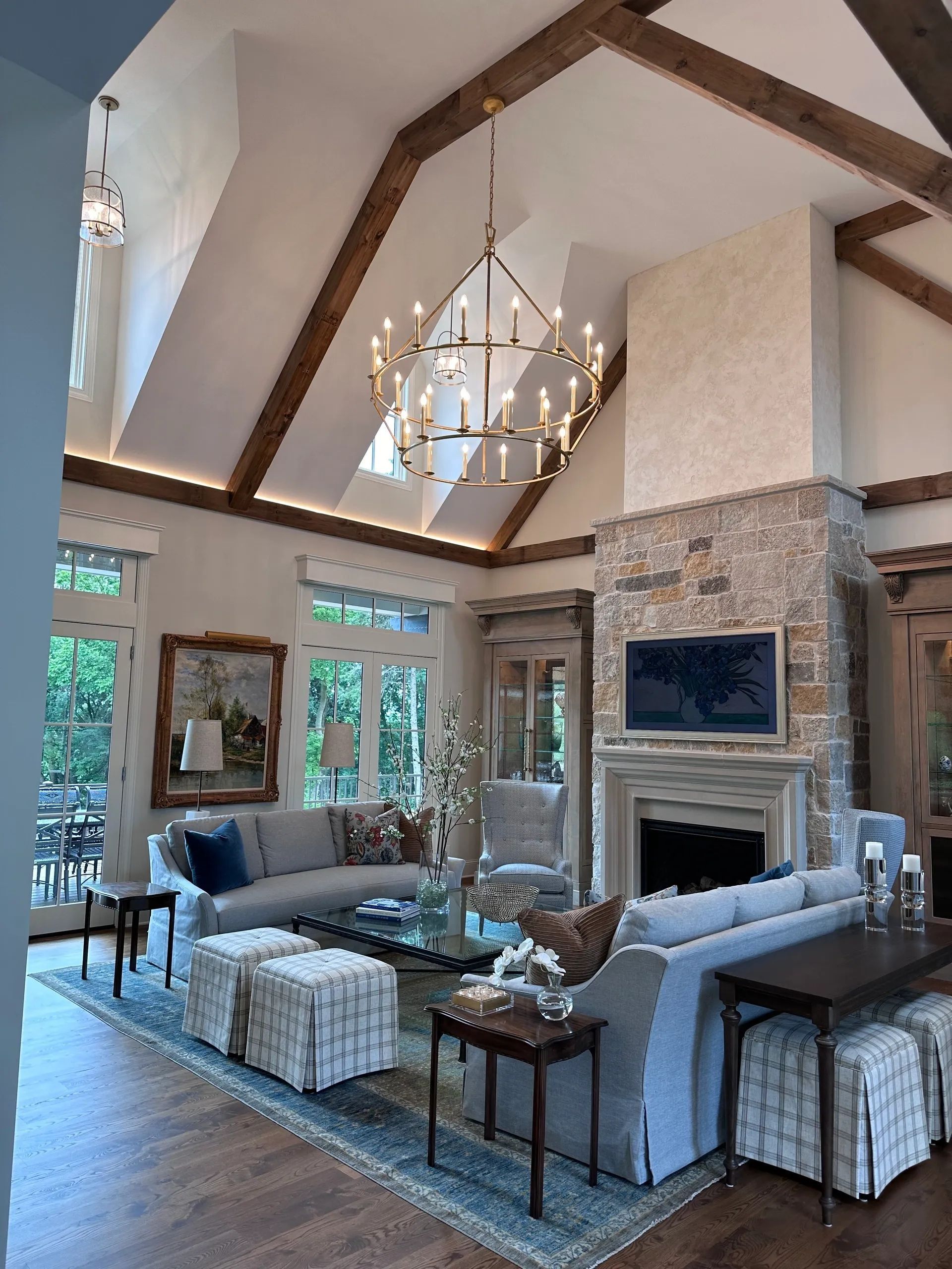 Living room with vaulted ceiling, stone fireplace, wooden beams, blue and gray furniture, chandelier.