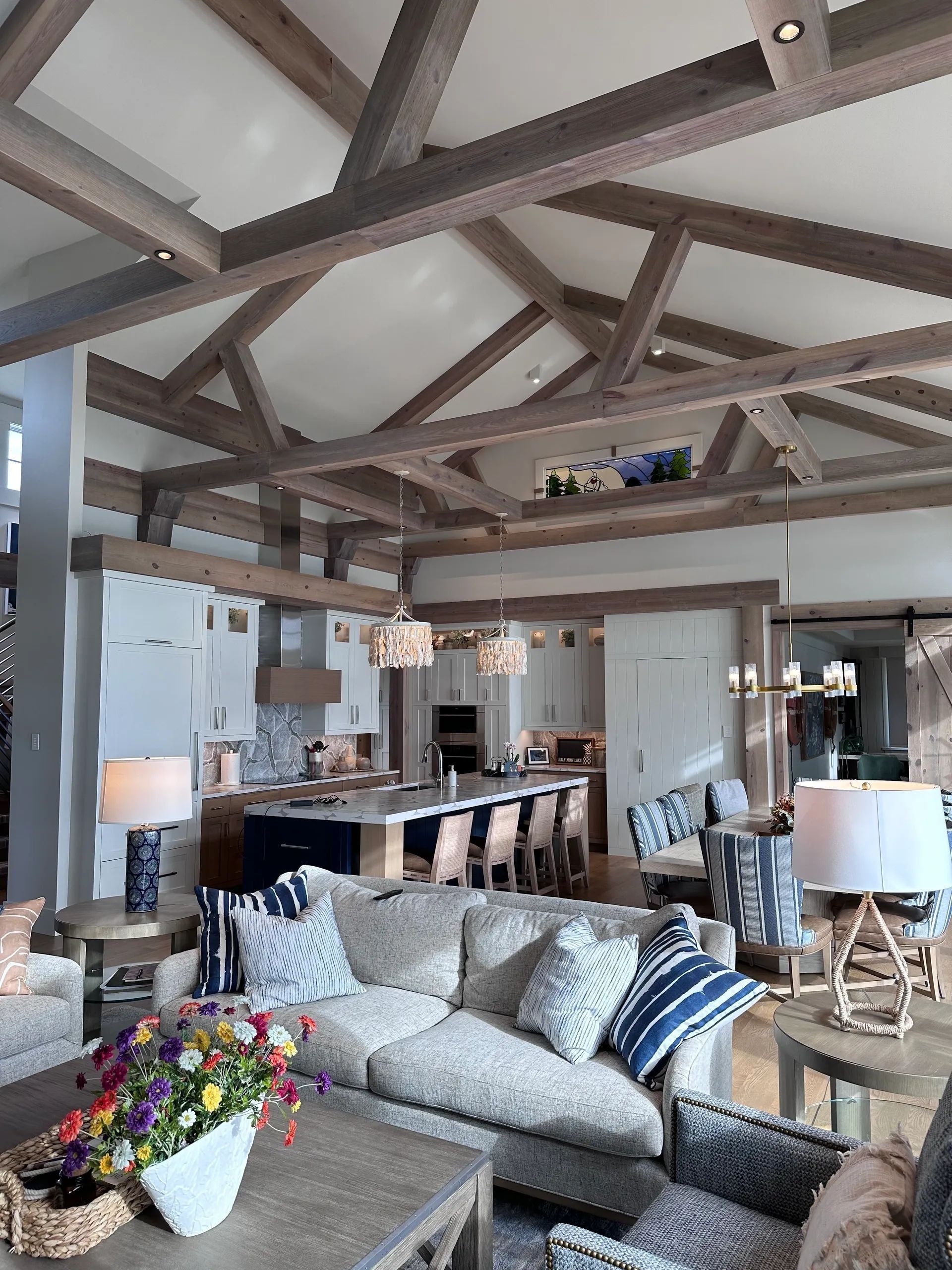 Living room with wood beam ceiling, open to a kitchen. Neutral tones with blue accents.