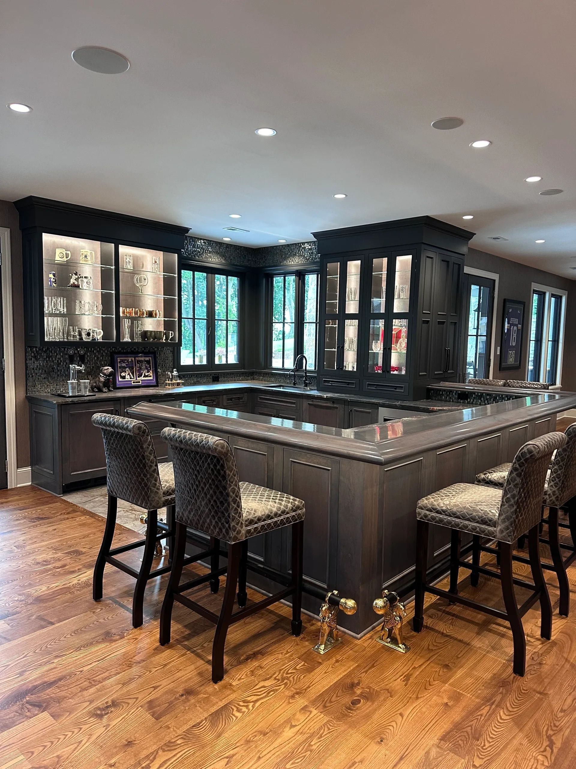 A home bar with dark wood cabinetry, a wrap-around countertop, and upholstered bar stools on a wood floor.t