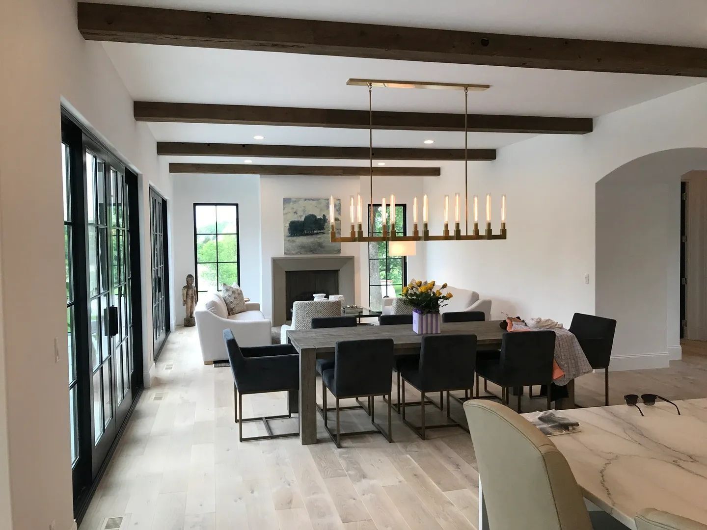 Dining room with wooden beams, large table and chairs, fireplace, and sliding glass doors.