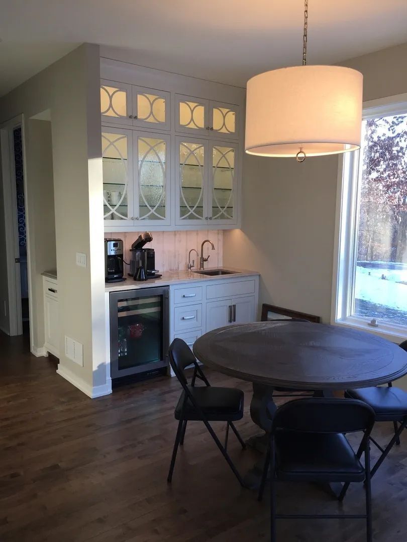 Built-in bar area with cabinets, sink, and wine fridge. Round table with chairs sits nearby.