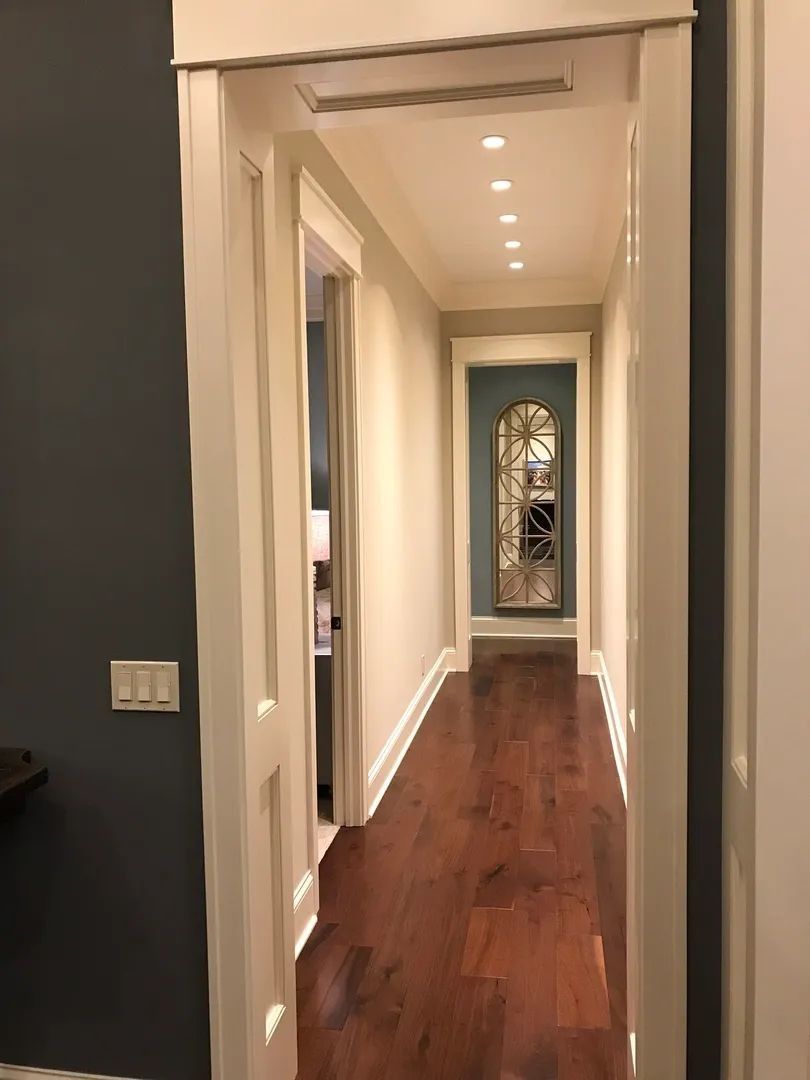 Hallway with dark wood floor, white walls and trim, and a turquoise door at the end.