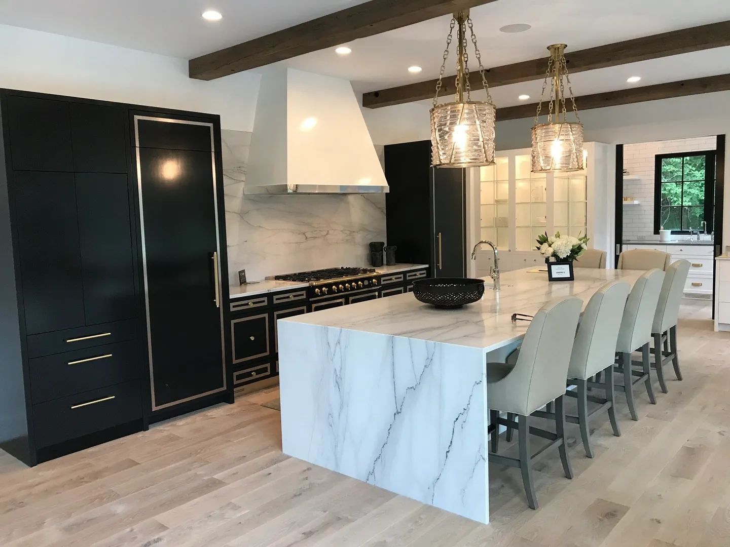 Luxury kitchen: black cabinets with gold trim, marble countertops, large island with seating, pendant lights, wood beams.